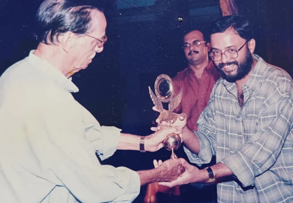 അഖില കേരള റേഡിയോ നാടകോൽസവത്തിന്റെ പുരസ്കാരം കാവാലം നാരായണപ്പണിക്കരിൽ നിന്ന് കെ.വി. ശരത്ചന്ദ്രൻ സ്വീകരിക്കുന്നു.